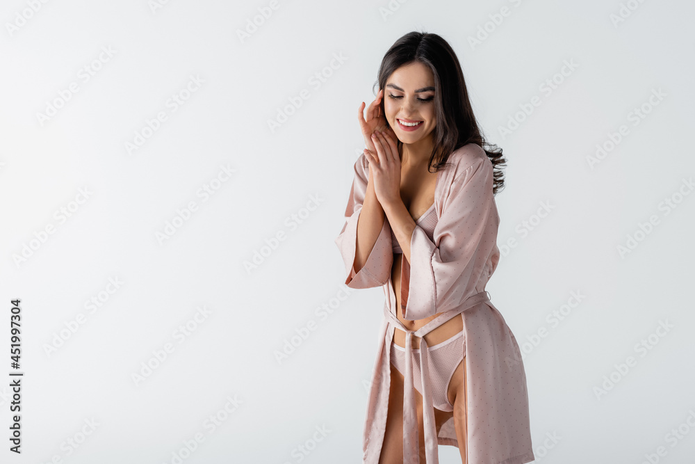 pleased young woman in underwear and silk robe looking down isolated on white