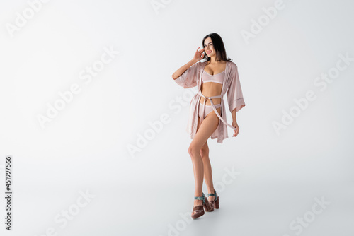 full length of cheerful young woman posing in underwear and silk robe on white
