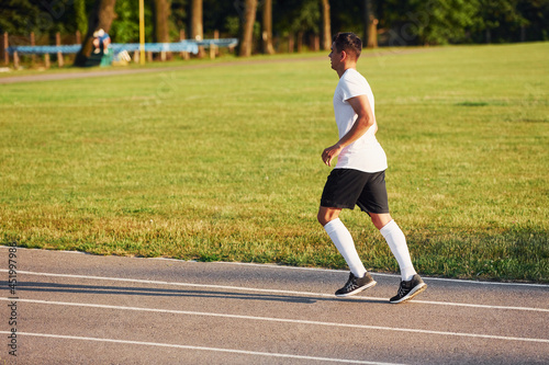 Man in sportive unifrom running on the track at daytime