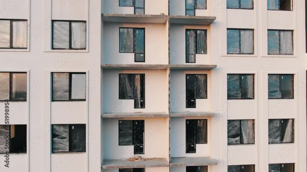 Motion upward unfinished pink building facade with unglazed windows and balconies to roof against distant city on horizon Motion upward unfinished pink building facade with unglazed windows and balconies to roof against distant city on horizon