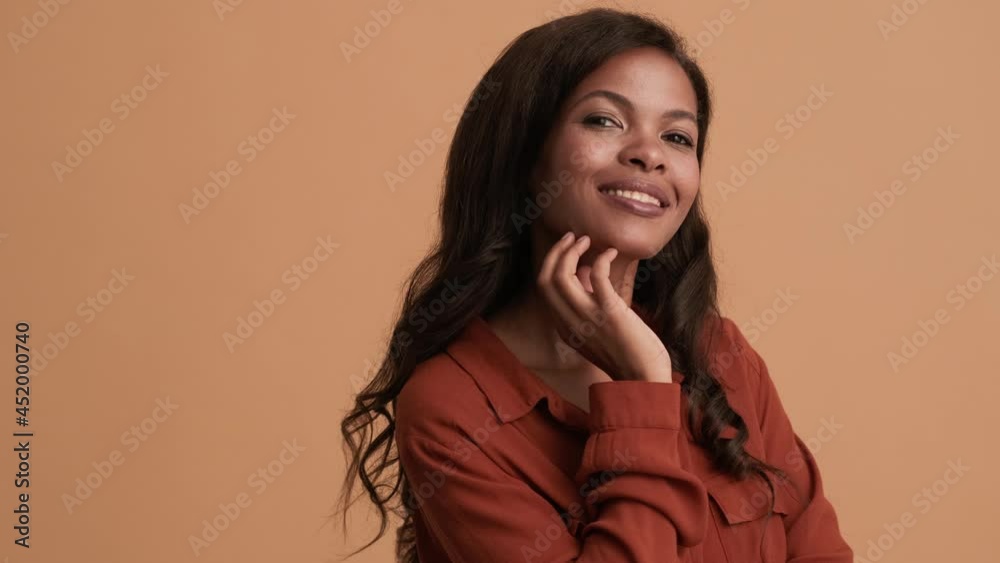 A charming brunette african american woman posing to the camera isolated over a beige background in the studio A charming brunette african american woman posing to the camera isolated over a beige background in the studio
