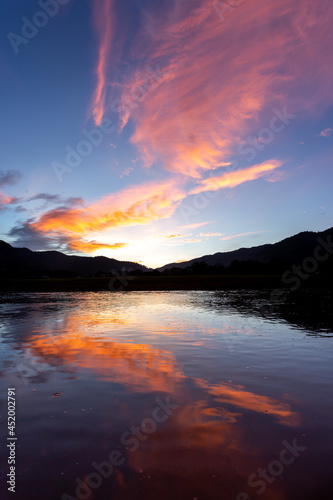 landscape silhouette The mountains, the sunset in the evening sky, and then the light hits the clouds is orange. There is a reflection in the river that feels relaxed There is space for text.