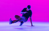Portrait of dancing man, break dancer in action, motion in modern clothes isolated over bright magenta background at dance hall in neon light.