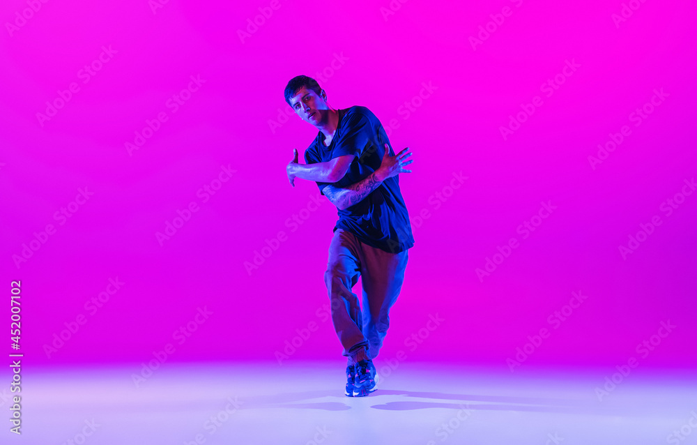 Young stylish man, hip-hop dancer dancing solo in modern clothes isolated over bright magenta background at dance hall in neon light.