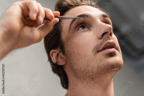 close up view of young man tweezing eyebrows in morning