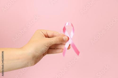 Female hand holds breast cancer awareness ribbon on pink background