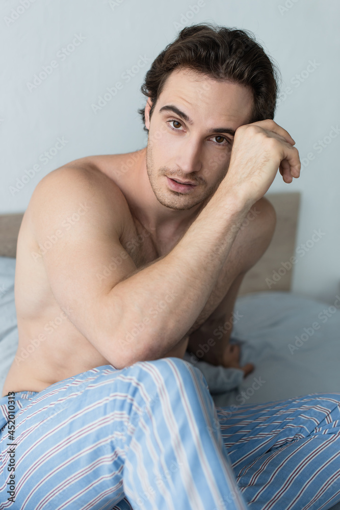shirtless man in striped pajama pants looking at camera in morning shirtless man in striped pajama pants looking at camera in morning