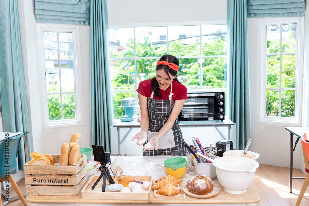 Beautiful Asian woman teaching how to make bread bakery and using a camera to record live broadcasts online on social media. Beautiful Asian woman teaching how to make bread bakery and using a camera to record live broadcasts online on social media.