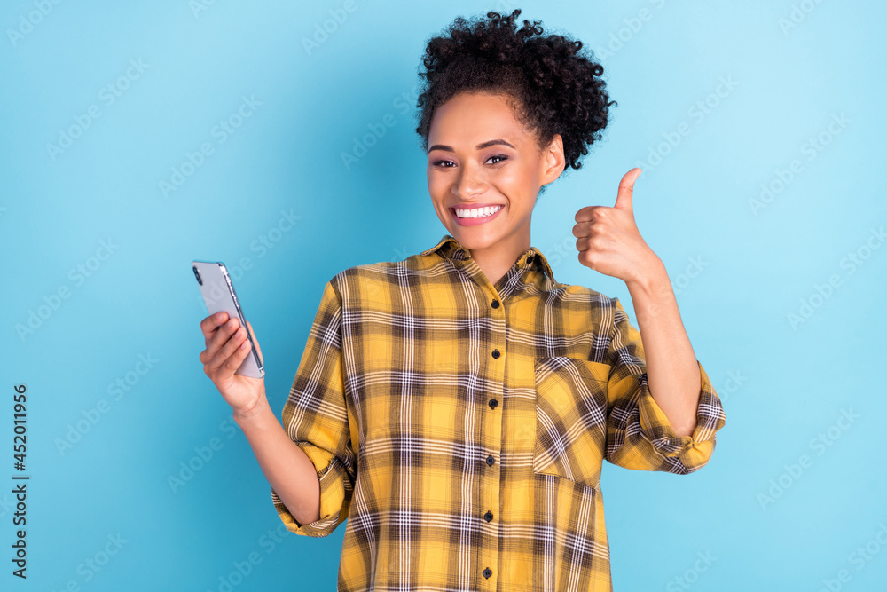 Photo portrait curly woman sshowing thumb-up keeping mobile phone isolated pastel blue color background Photo portrait curly woman sshowing thumb-up keeping mobile phone isolated pastel blue color background