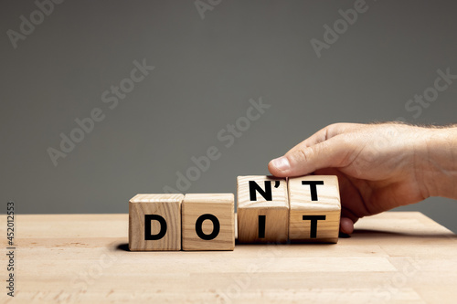 Foto Male hand flips wooden cubes with words DO IT to DON'T on the table over grey background