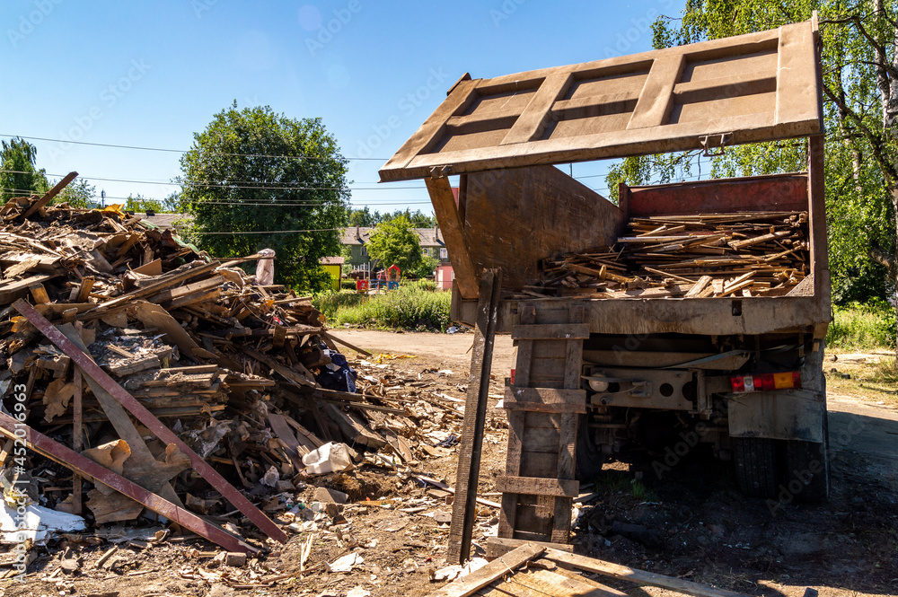 the wreckage of a dismantled wooden house is loaded into the back of a garbage truck