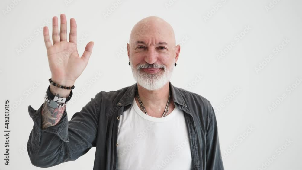 A positive bald mature man doing hello gesture standing isolated over white background in the studio A positive bald mature man doing hello gesture standing isolated over white background in the studio