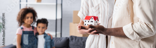 african american couple holding house model near blurred kids in new apartment, banner