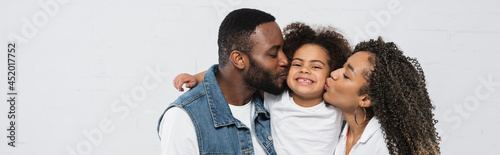 happy african american couple kissing daughter on grey, banner