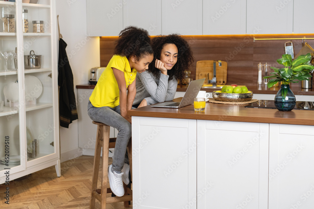 Mother and daughter using laptop together in kitchen. Mother and daughter using laptop together in kitchen.
