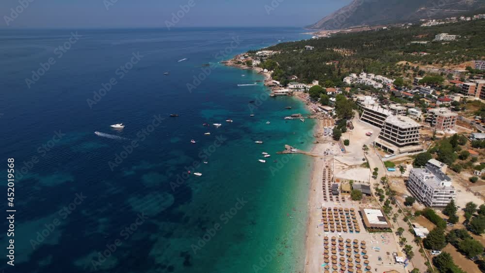 Tour boats floating near pier at beautiful beach of Dhermi in Albania, row of umbrellas near blue turquoise sea Tour boats floating near pier at beautiful beach of Dhermi in Albania, row of umbrellas near blue turquoise sea