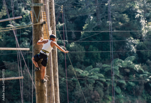 Man standing at top of poll ready to balance on suspended rope at outdoor ropes course photo
