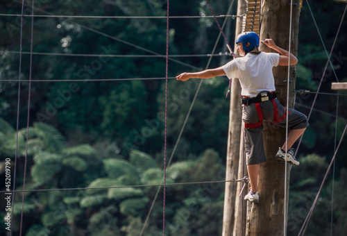 Woman standing at top of post ready to balance on suspended rope at outdoor ropes course photo