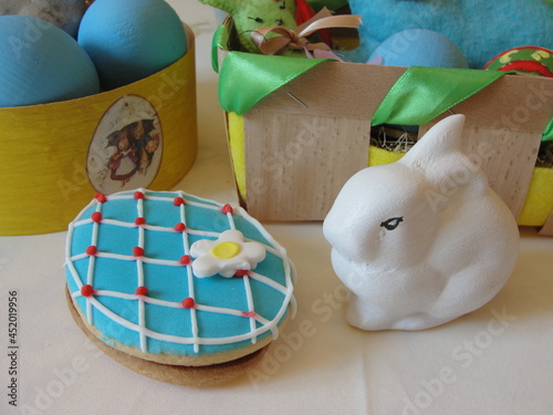 Ceramic figurine of a rabbit, a gingerbread with a decor and baskets with Easters crafts on a table. Easter decor. 