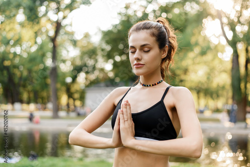 Calm young woman practices yoga and meditation while standing in the park. Outdoor sports