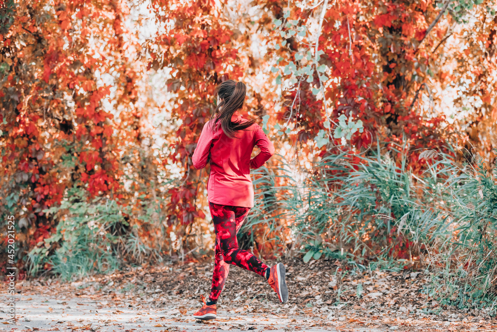 Running woman jogging on autumn red leaves foliage background. Fall cardio exercise training. Happy athlete runner exercising outdoor.