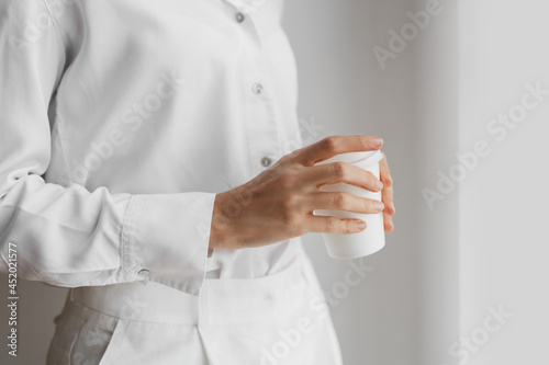 Unrecognizable woman in white shirt holding coffee cup.