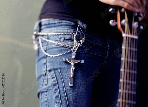 Mid section of young woman wearing a crucifix and chain around her waist and holding a guitar