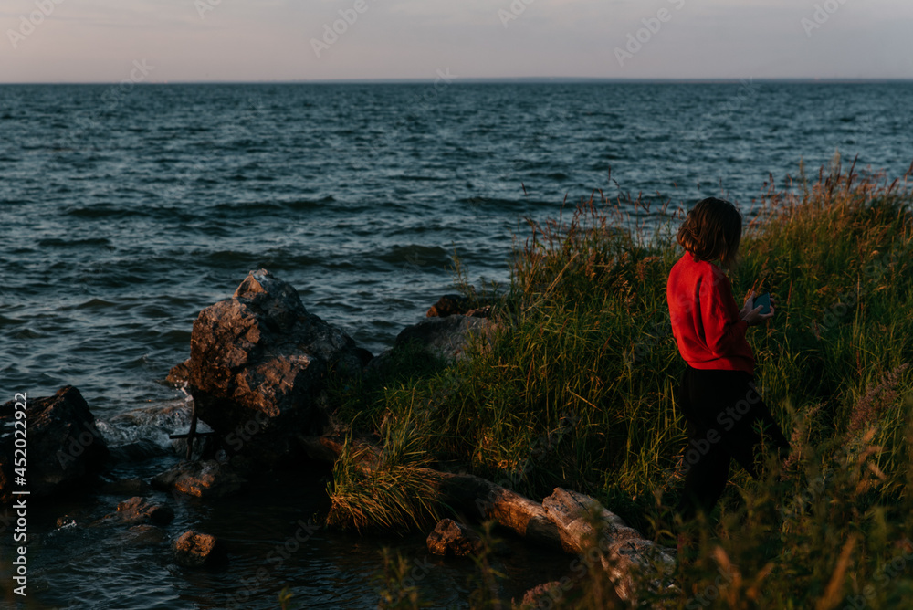 Photo  of a Summer Camping Activity. Travel location of popular tourist outdoor. View of beautiful Sea Landscape and Woman make selfie. Vacation by the lake in a camp with a bonfire and tent