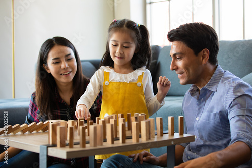 Obraz na plátně Mix race family lovers, Caucasian dad and Asian mom with half-blood daughter playing wooden domino game together in living room with happy and fun