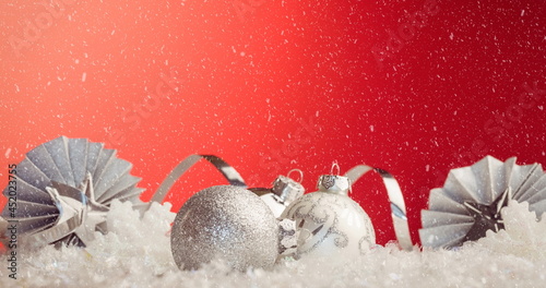 Image of white christmas baubles decorations with snow falling on red