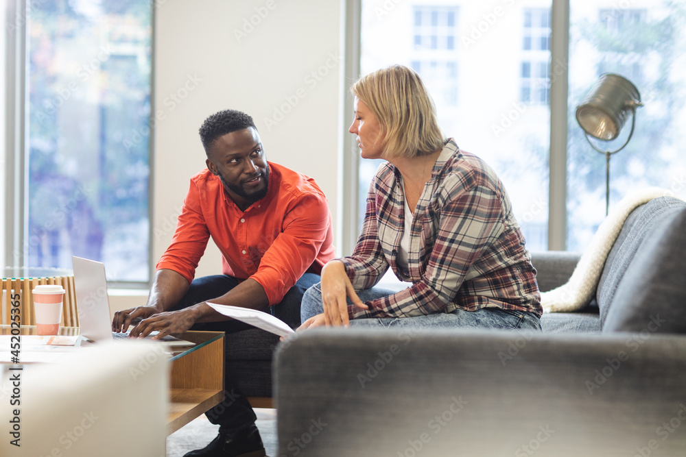 Smiling diverse female and male colleagues sitting on sofa at workplace ...