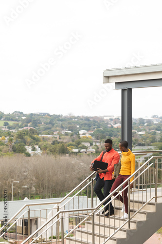 Wallpaper Mural Smiling african american male and female creative colleagues walking downstairs and talking Torontodigital.ca
