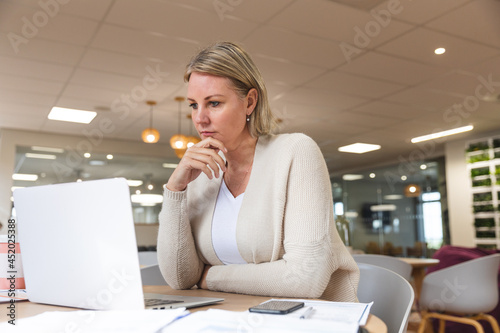 Thoughtful caucasian female business creative using laptop at workplace cafeteria photo