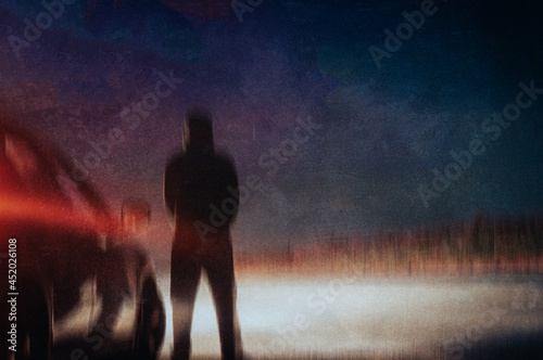 A spooky hooded figure, back to camera, silhouetted against a cars headlights. On a country road at night. blurred, texture edit