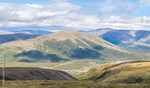 Panoramic view of the mountain range. Cloudy sky and green tunra. Cloud shadows on mountains covered with dwarf birch and mosses