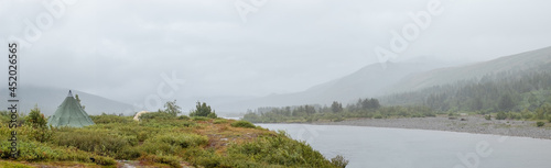 Rainy day on the Sob river in the Ural mountains. Tourist tents in anticipation of good weather. Mountains hidden by fog.