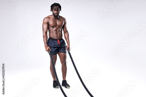 slim well-built afro american athlete preparing for training with battle ropes, full-length portrait, isolated white background, studio shot. bodybuilding, cross fit, weightlifting, sport, fitness