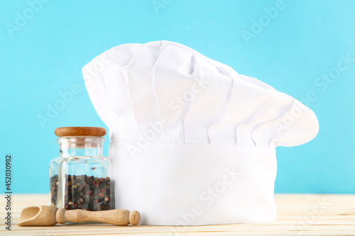 Chef hat with spices in jar and wooden scoop on blue background