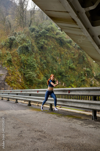 Young woman running jogging fast outdoors. Female athlete exercising on modern bridge. Side view on strong active vigorous lady in blue sportswear running forward  copy space. sport concept