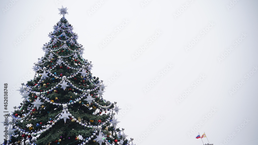 Christmas tree on evening street. Low angle of coniferous tree with traditional Christmas decorations located on street in evening in city