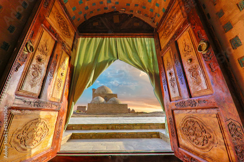 Photographie View over the mausoleum through wooden doors at the sunset, in the ancient cemet