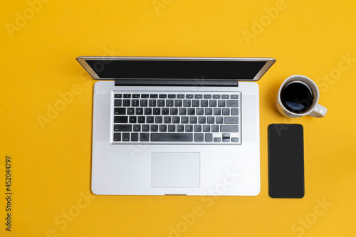 top view of laptop, cup of coffee and mobile phone on yellow isolated background. office