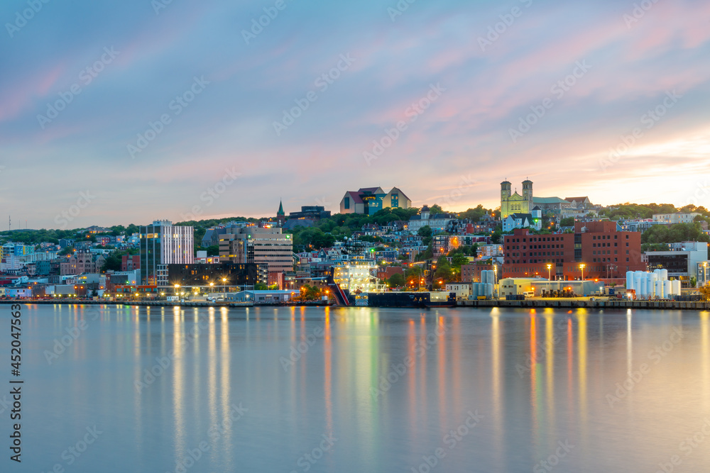 St. John's, Newfoundland, waterfront harbour at sunset. The lights on the water are bright yellow and orange which are reflecting from the skyline in the stillness of the smooth water.  