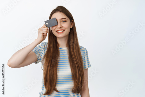 Beautiful smiling girl shows her credit card, discount coupon, standing against white background