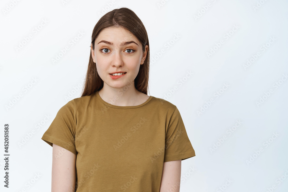 Hopeful and excited girl, biting lip and looking at camera with anticipation, waiting to receive smth, standing over white background Hopeful and excited girl, biting lip and looking at camera with anticipation, waiting to receive smth, standing over white background