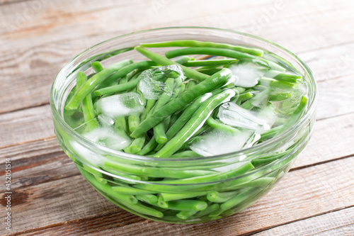 Green beans in a colander. Boiled or blanched vegetables in ice water on a table photo