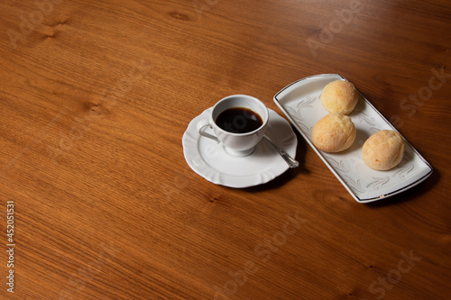 black coffee served in white cup and saucer, beside cheese bread in white rectangular plate on wooden table.