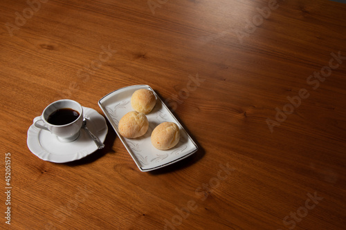 small black coffee served in white cup and saucer, cheese rolls served on white square dinnerware, wooden table, photo taken from above, space for text