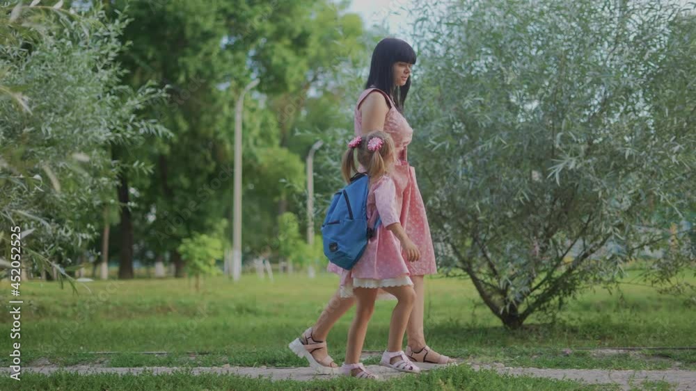 back to school. mom daughter schoolgirl walk by the hand in the park with a backpack. back to school education concept. little girl daughter with a backpack and road mom are walk in the park back to school. mom daughter schoolgirl walk by the hand in the park with a backpack. back to school education concept. little girl daughter with a backpack and road mom are walk in the park