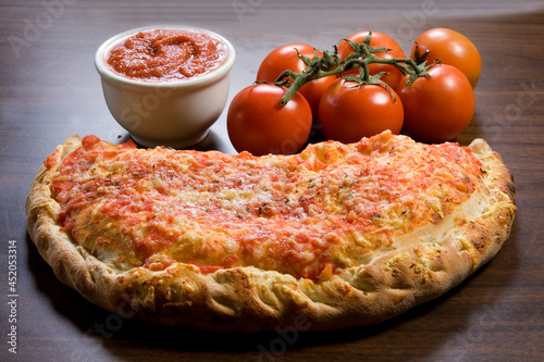 Fogazza fechada, comida típica italiana, em fundo de mesa com adorno de tomates e molho de tomate. photo